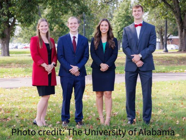 A group photo of male and females in professional attire on a campus green setting with the words
